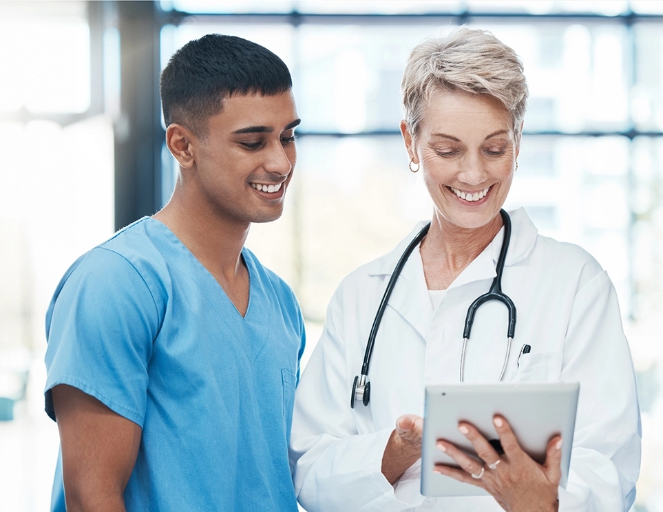 a man and woman wearing scrubs looking at a tablet